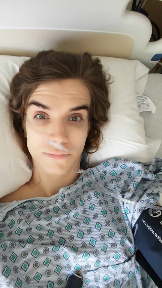 Sami D laying in bed shortly after surgery in a blue hospital gown.